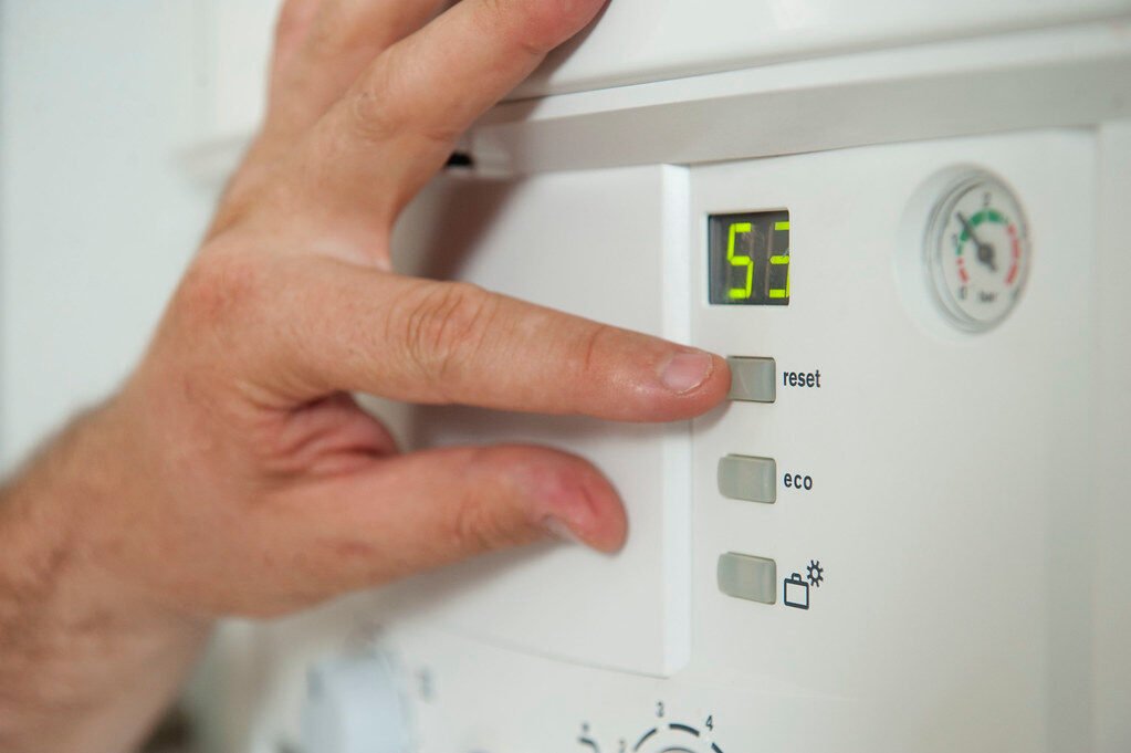 Close-up of hands adjusting a boiler system with precise instrumentation, showing maintenance work.